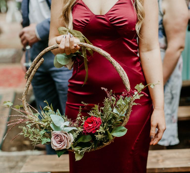 Bridesmaid in a fitted red satin bridesmaid dress holding a floral hoop bouquet 