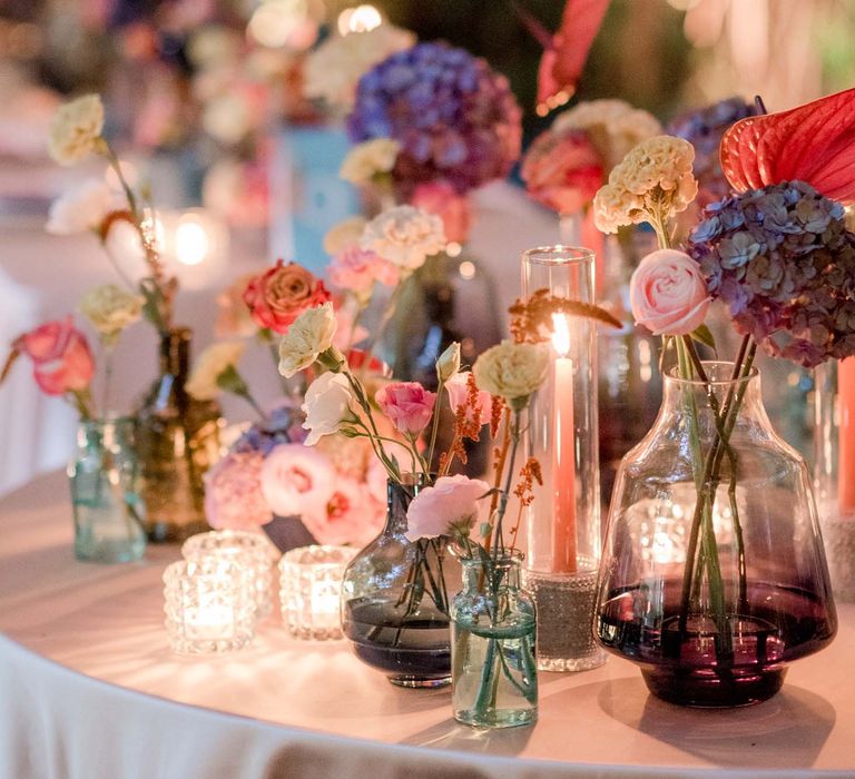 Colourful tablescape complete with coloured glasses and vases filled with bright florals