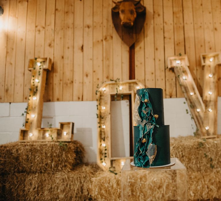 Big wooden letters spelling 'LOVE' on hay bales and blue two tier wedding cake for rustic farm wedding