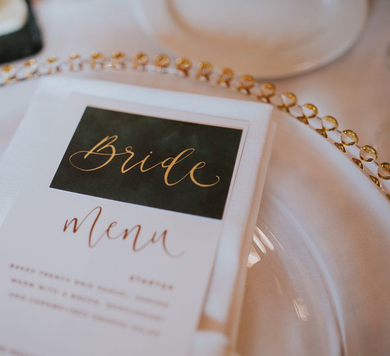 Green table place name with gold calligraphy spelling 'Bride' with Menu on white and gold plate for Notley Abbey wedding