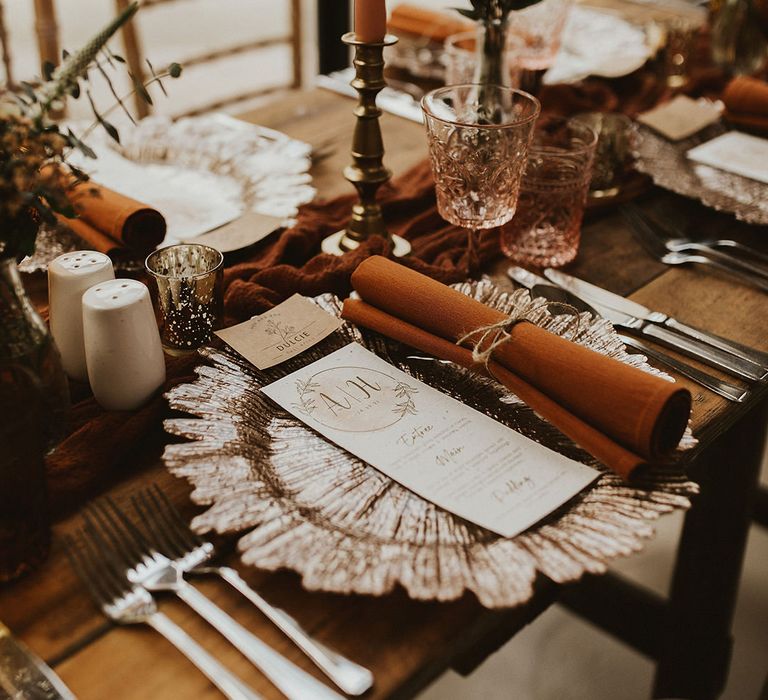 Beautiful wedding table place setting with rust napkins and gold candlesticks