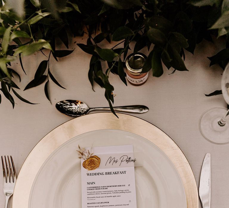 Place setting with gold rimmed plate, menu and place card with gold wax seal and wedding favour 