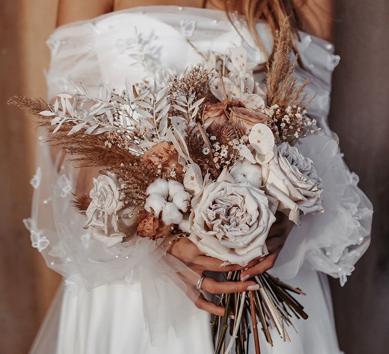 Bride in a strapless wedding dress holding a dried flower wedding bouquet with roses 