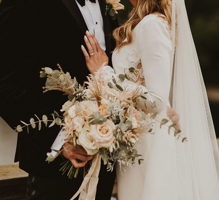 Groom in a tuxedo kissing his bride in a long sleeve wedding dress, pearl headband and cathedral length veil