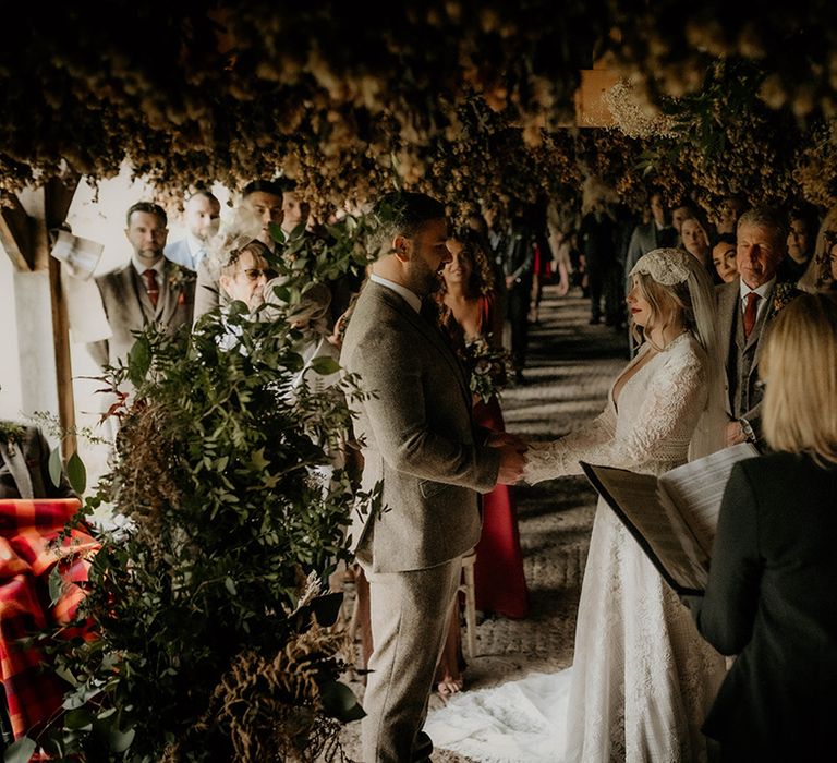 Autumnal wedding ceremony at Lyde Court with groom in a wool suit exchanging vows with his bride in a lace wedding dress with long sleeves