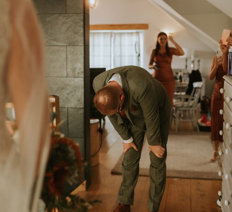 Wedding guests in green suit stands with hands on knees after first look