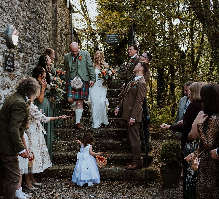 Bride & groom walk down staircase as wedding guests throw confetti around them