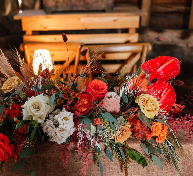 Mixed rustic wedding florals with roses and dried grasses in reds, oranges and greens