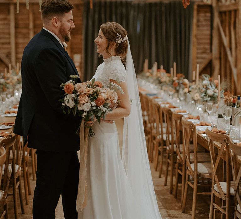 Bride clutches blush and orange bouquet as she looks at husband