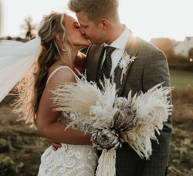 Bride clutches pampas grass bouquet as she kisses groom