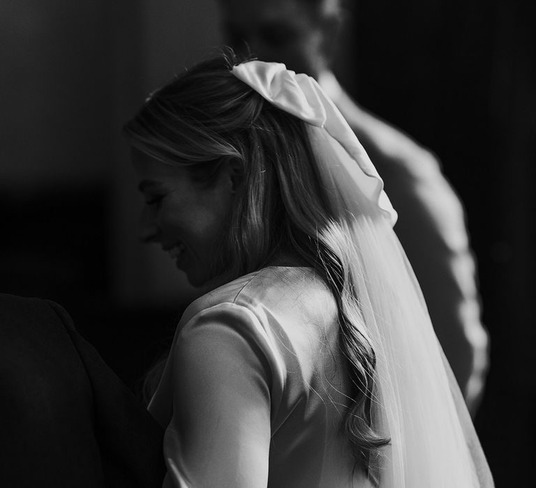 Bride in satin wrap top, satin hair bow and veil walks up the aisle for church wedding ceremony