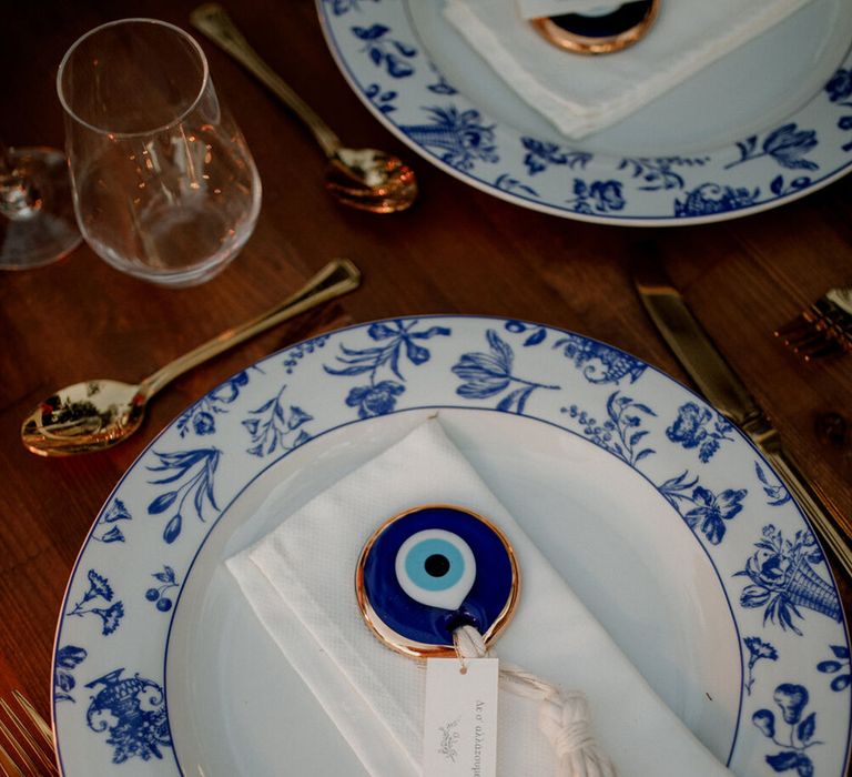 White & blue china plates complete with evil eye decorative piece on white napkin 