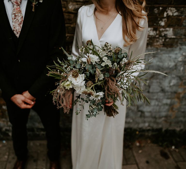 Bride holds floral bouquet as she stands with her groom