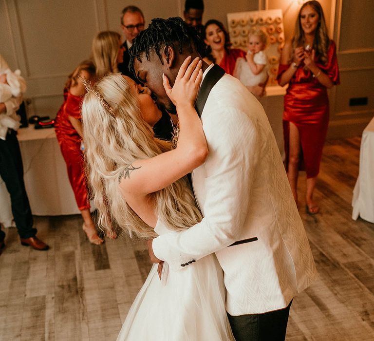 Bride and groom kiss in front of guests and doughnut wall