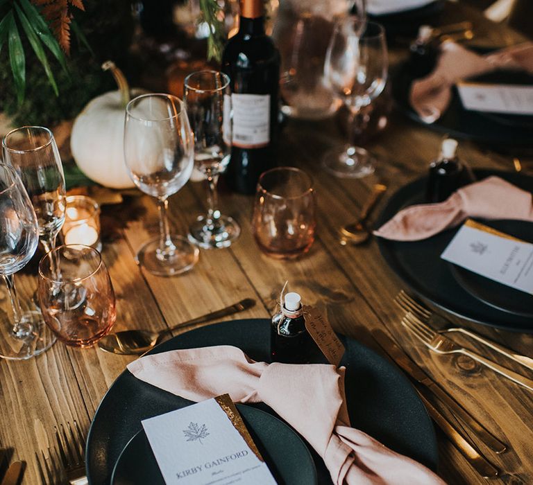 Place setting with black tableware, pink napkins and gold guilt menu card for autumn theme wedding 