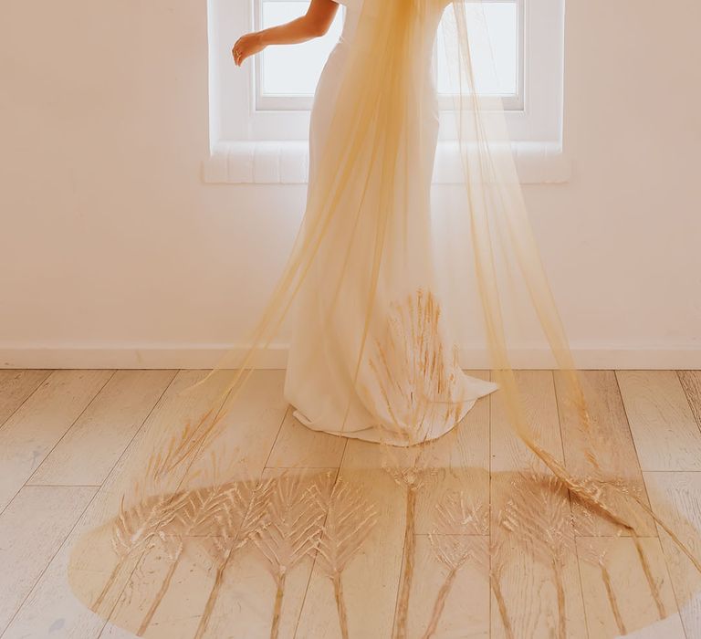 Black bride in an off the shoulder wedding dress with afro hair wearing a golden patterned wedding veil 