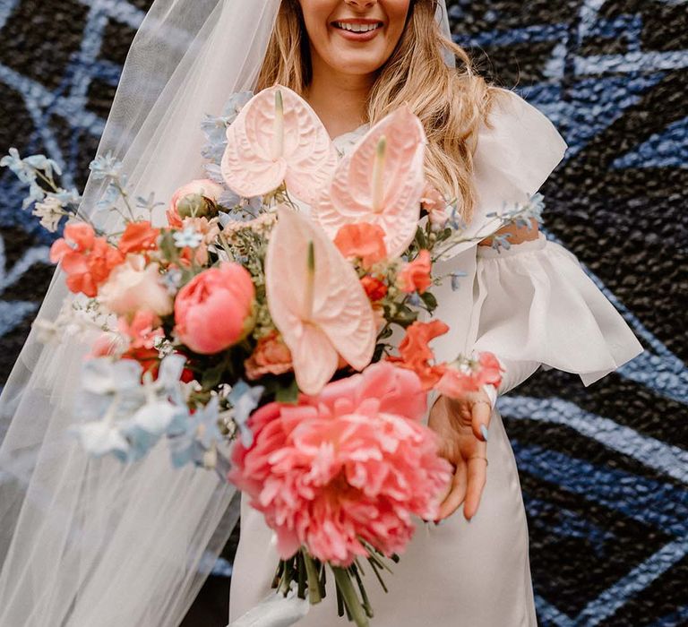 Fun wedding elopement with bride holding a coral pink and blue wedding bouquet with peonies, anthuriums and delphiniums