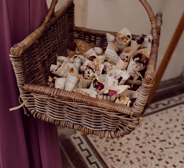 Bridesmaid in deep purple dress holds wicker basket of wedding confetti in music paper cones 