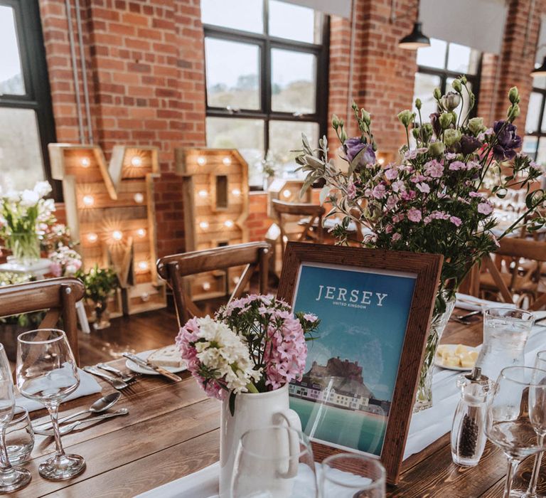 White jug vase full of white and pink hyacinth next to photo frame with picture and name of the table with white table runner and large light up Mr & Mrs sign