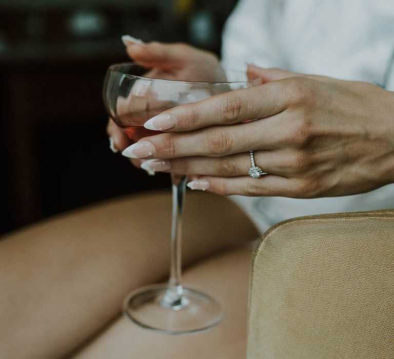 Bride with almond shape French tip nails with pearls holding cocktail glass with pave round diamond engagement ring 