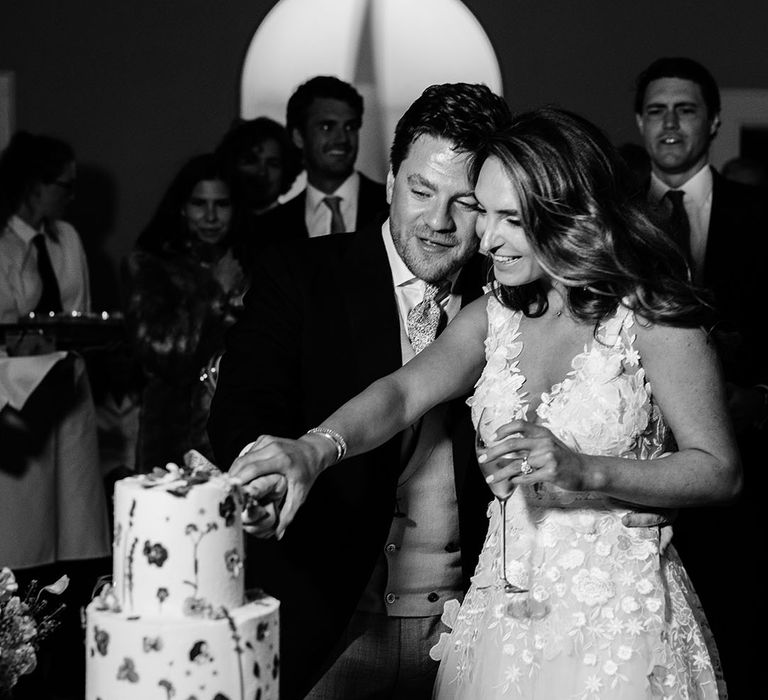 Bride and groom cut their three tier wedding cake with flowers 