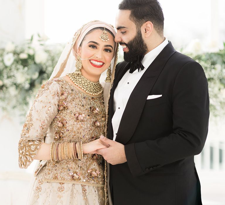 Bride wears traditional saree in gold and silver whilst leaning into her groom who wears black tie for Nikkah & Walima 