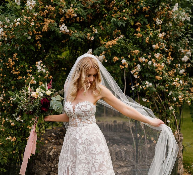 Bride holding red and white wedding bouquet tied with pink ribbon with veil and strapless lace wedding dress 