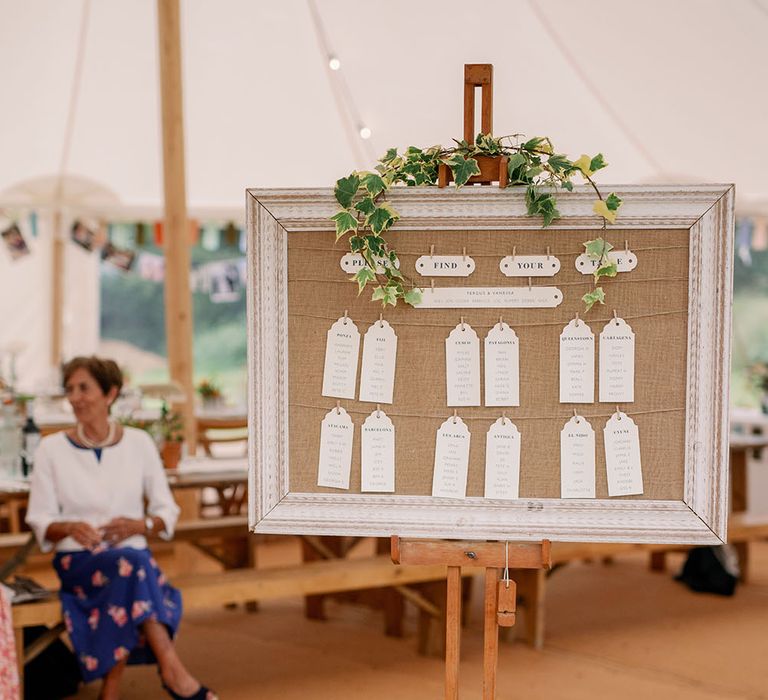 DIY table plan sits at the front of marquee surrounded by white floral decor 