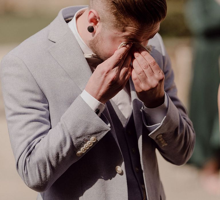 Groom wearing pale grey three piece suit becomes emotional seeing his bride for the first time during wedding ceremony