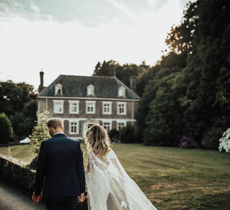 Groom walks with the bride in a sheer lace wedding cape 