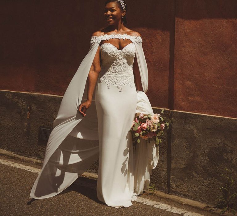 Bride wearing a plain white bridal cape in an off the shoulder style with floral design 