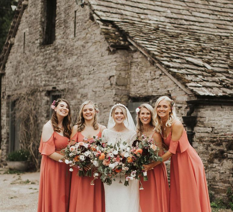 Bridal party shot with the bridesmaids in coral bridesmaid dresses and bride in a lace wedding dress