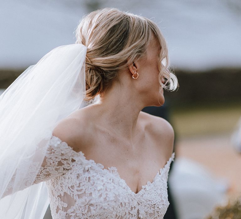 Bride with blonde hair in an updo wearing a lace long sleeve wedding dress and gold hoops 