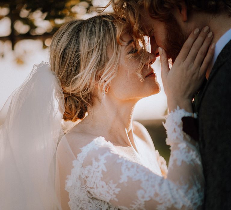 Bride in lace long sleeve wedding reaches and cups the groom's face 