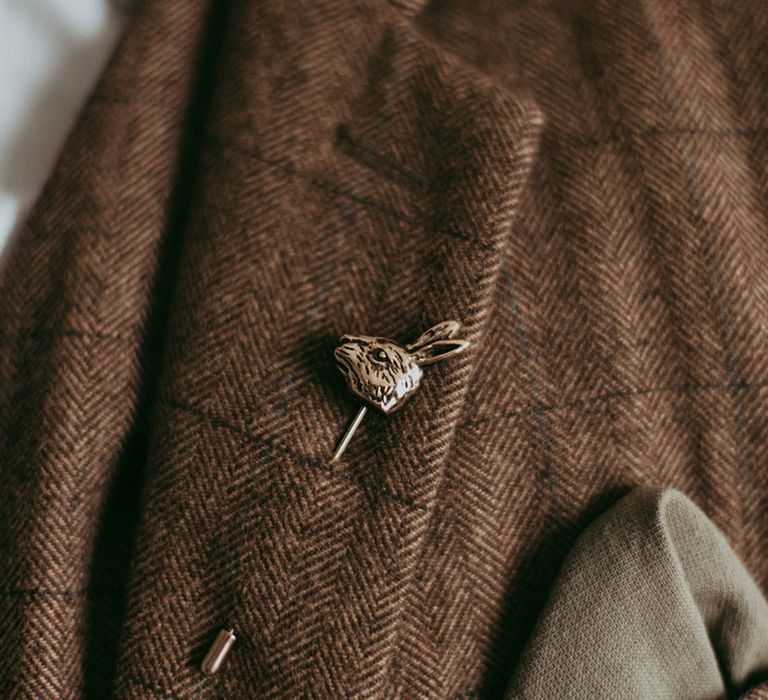 Groom in brown checkered suit with a gold rabbit pin and green handkerchief 