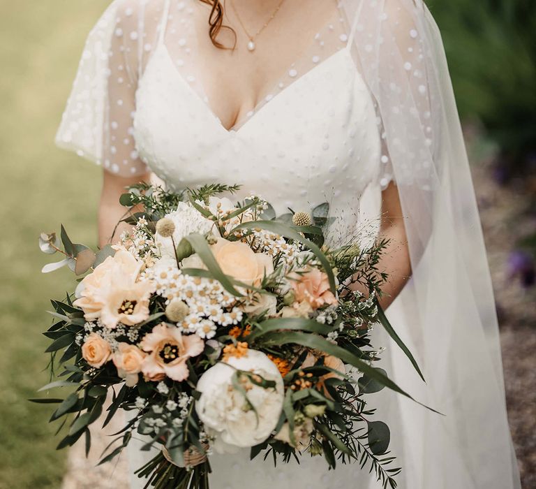 Bride wearing a pearl drop necklace, dotted wedding dress and a quartz crystal crown holding a white and peach wedding bouquet