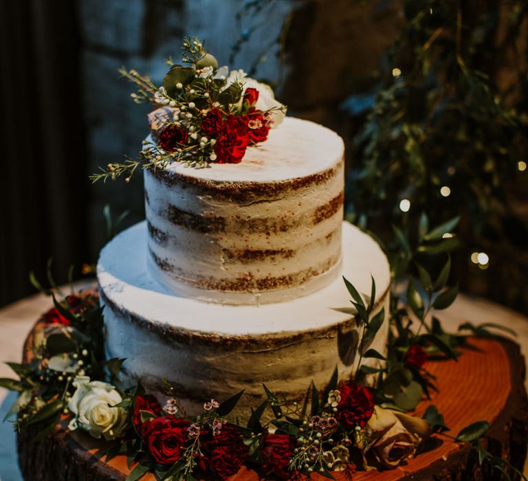 Semi-naked rustic wedding cake with white icing and white and red flower decor 