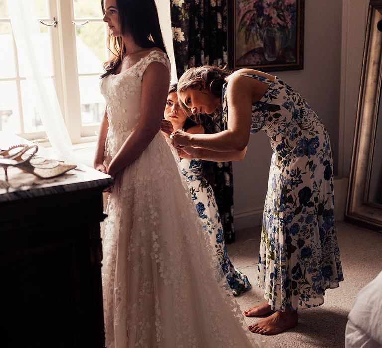 Bridesmaids in blue flora dresses help the bride get into her Phillipa Lepley applique wedding dress