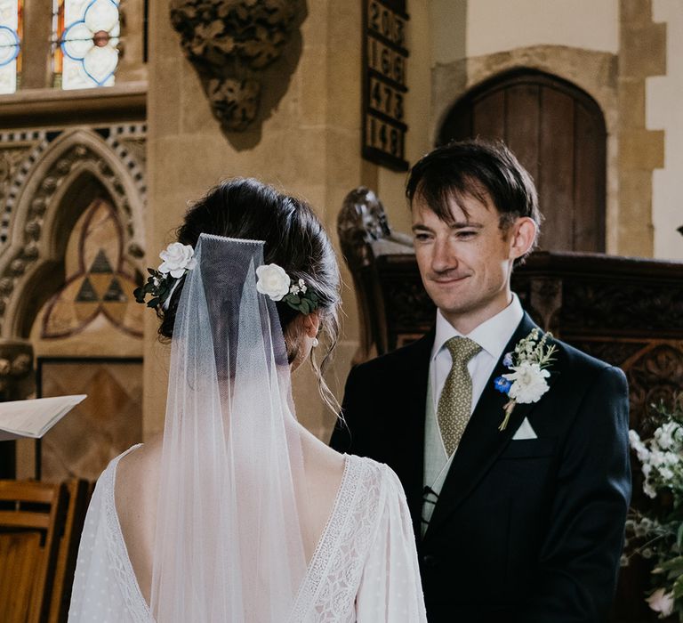 Bride in batwing sleeve and polka dot detail wedding dress dancing with neutral toned bridal bouquet and groom in dark three piece suit standing at the alter giving their vows