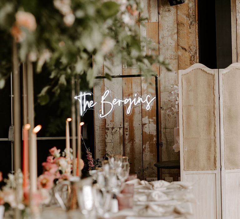 Personalised neon wedding sign hangs in front of wooden wall 