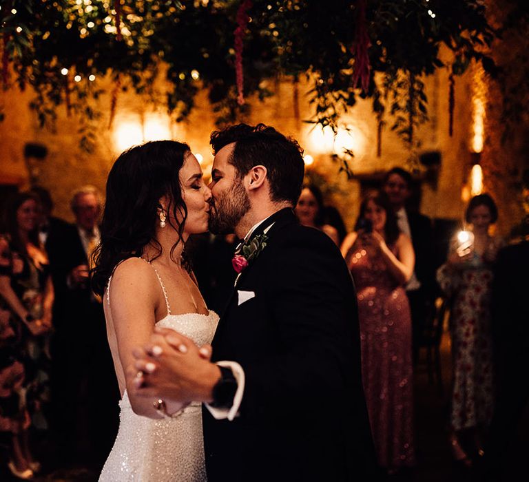 Wedding guests watch on as the bride and groom share their first dance together and kiss 