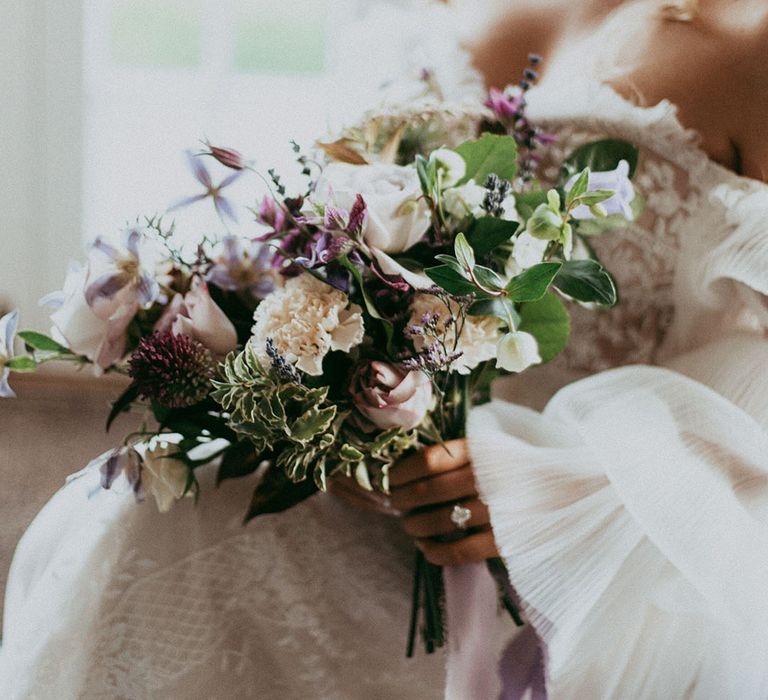 Bride holding mixed neutral floral bouquet with white carnations, purple tulips, roses and foliage 