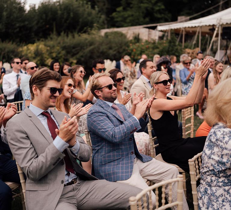 Wedding guests seated at the outdoor wedding ceremony starts applauding for the bride and groom 