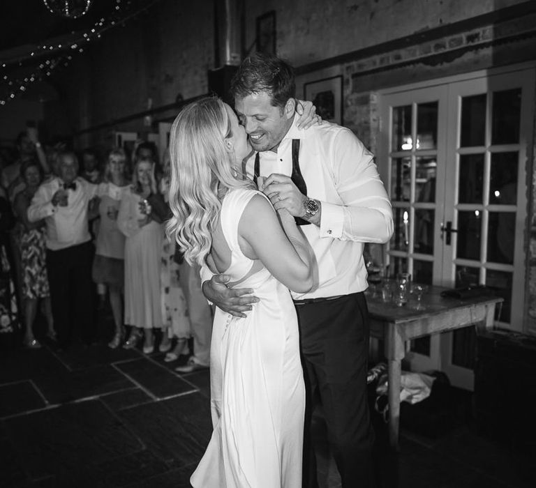 Bride in a white satin wedding dress sharing her first dance with the groom wearing his bow tie undone 