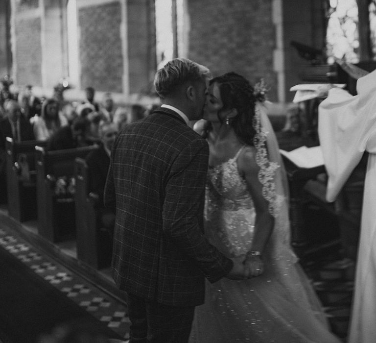 Black and white shot of the bride and groom as they share their first kiss as a married couple at their church wedding ceremony 