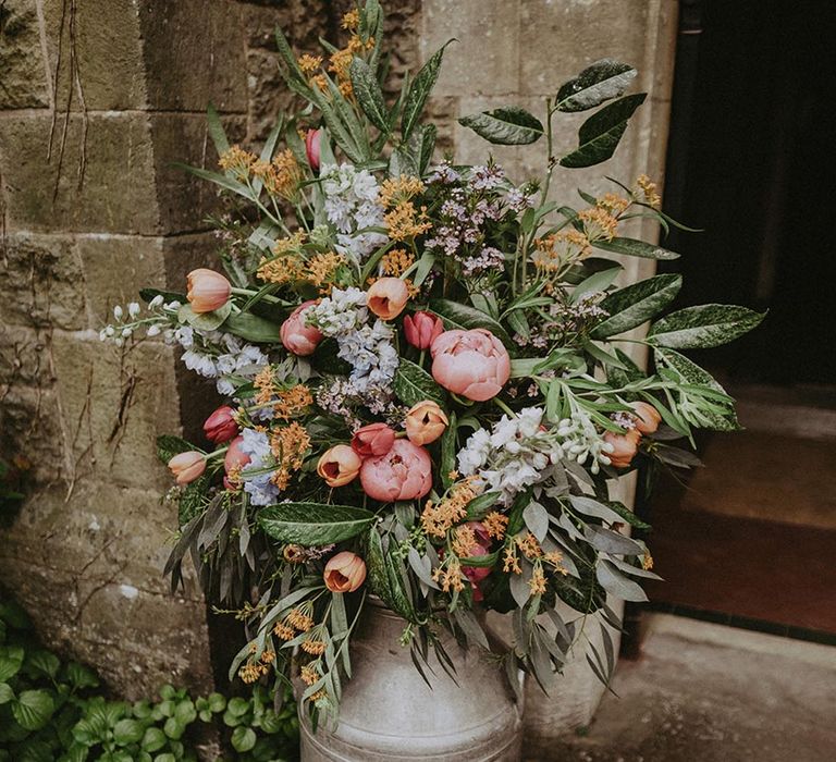 Milk churn wedding flower arrangement with tulips and peony with dark green leaves 