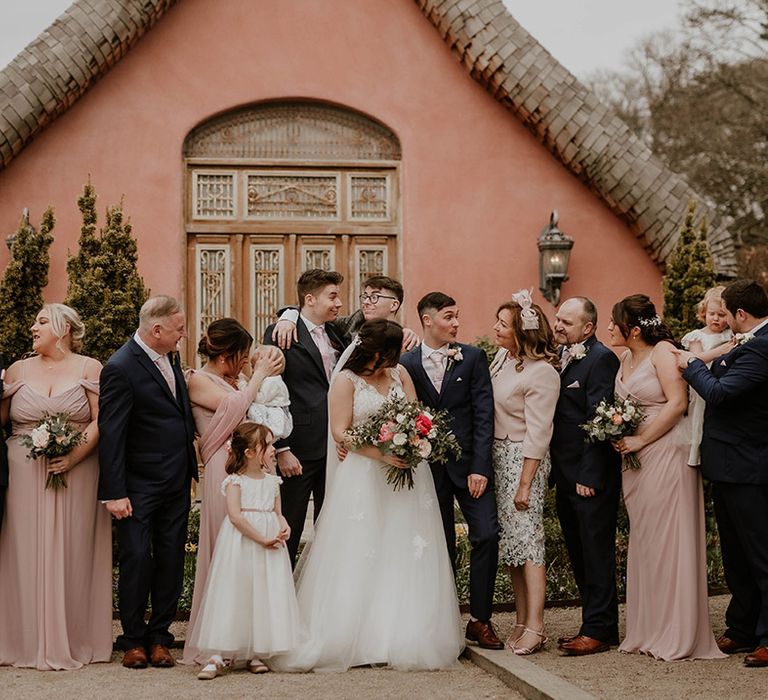 Bride & groom stand with their wedding party with bridesmaids wearing pale pink bridesmaid dresses 