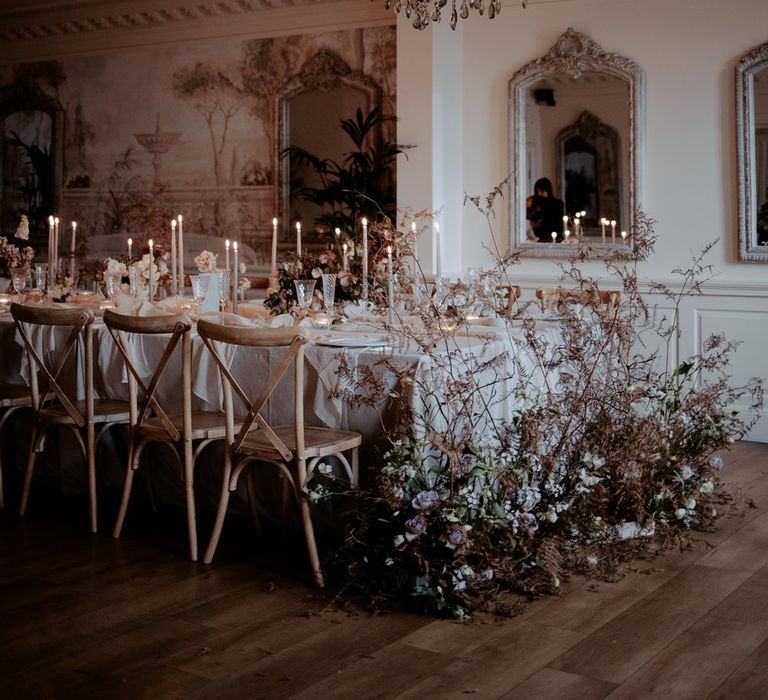 Reception room of Eaves Hall Clitheroe with large dark chandelier, large dark dried flower and rose floral arrangements, beige tapered candles and white table runners 