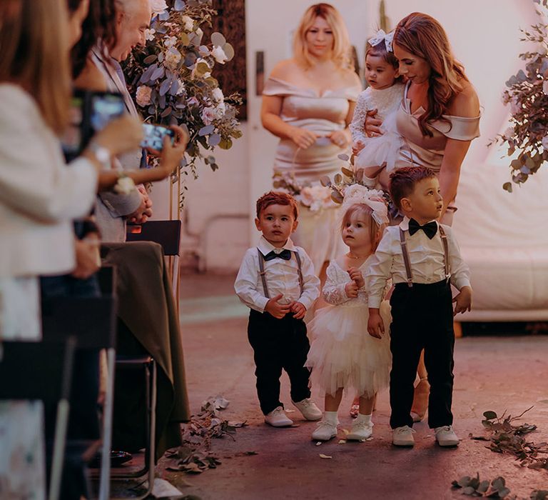 Flower girls in off white tutus and large hair bows and page boys in white shirts, suspenders and black bowties 