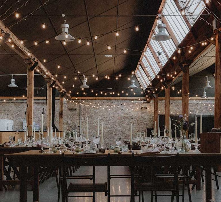 Industrial styled reception venue complete with festoon lighting and wooden banquet tables with DIY florals 